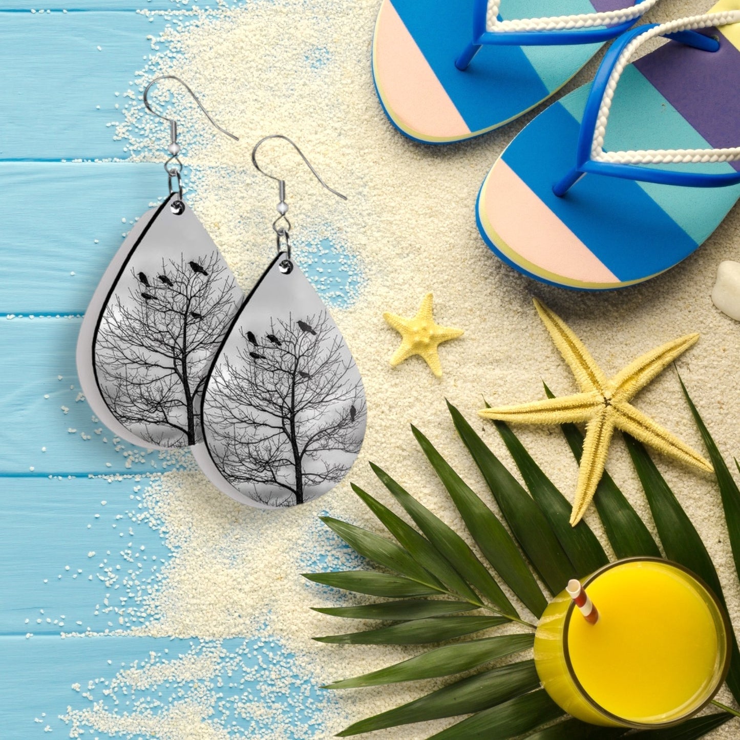 Teardrop-shaped earrings with tree design on a beach-themed background with flip-flops, starfish, and a drink.
