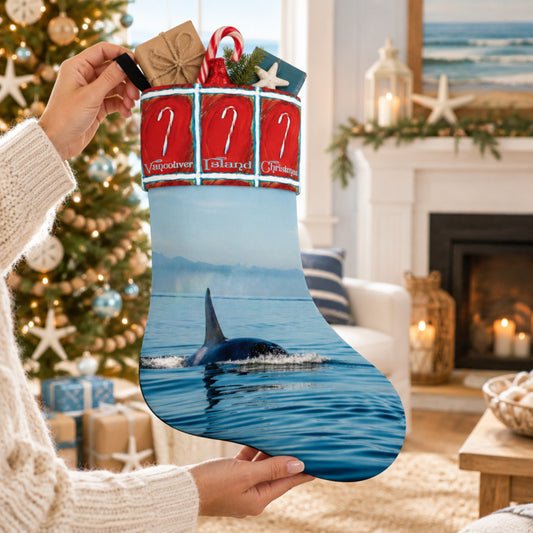 A person holds up a Christmas stocking in a cozy living room setting. The stocking features a printed design of an orca whale swimming in blue water, with a red and white striped top section containing candy cane graphics and the words 'Vibrant Life'.