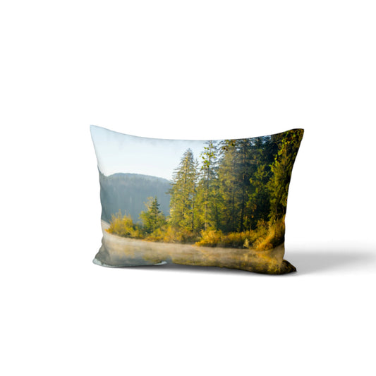 A rectangular throw pillow featuring a scenic landscape print of a misty forest road with pine trees, yellow-green foliage, and distant hills under a pale sky, shown on a clean white background.