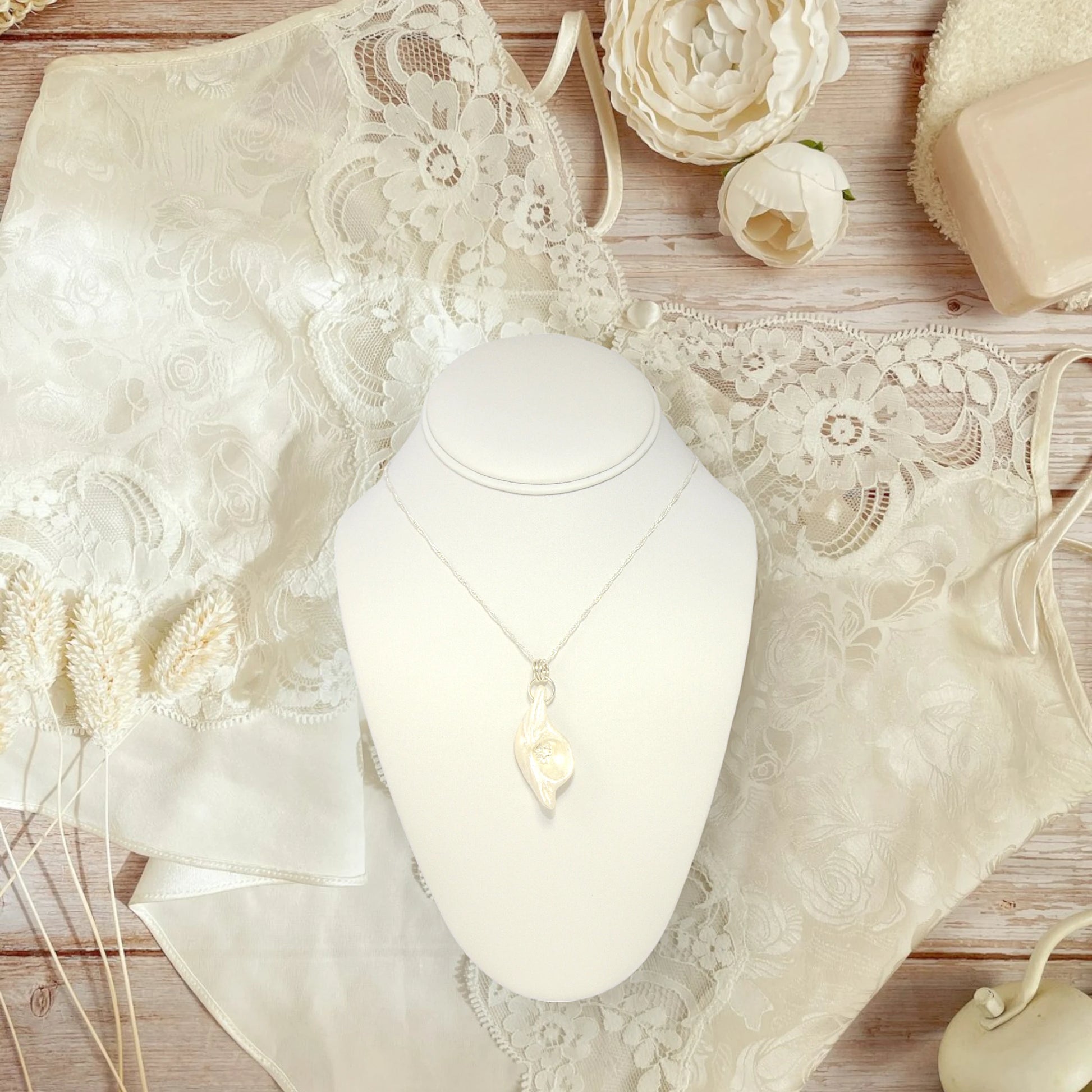 Halo natural seashell pendant with three herkimer diamonds. The pendant is shown hanging on a necklace displayer with a lace camisole and flowers in the background. 