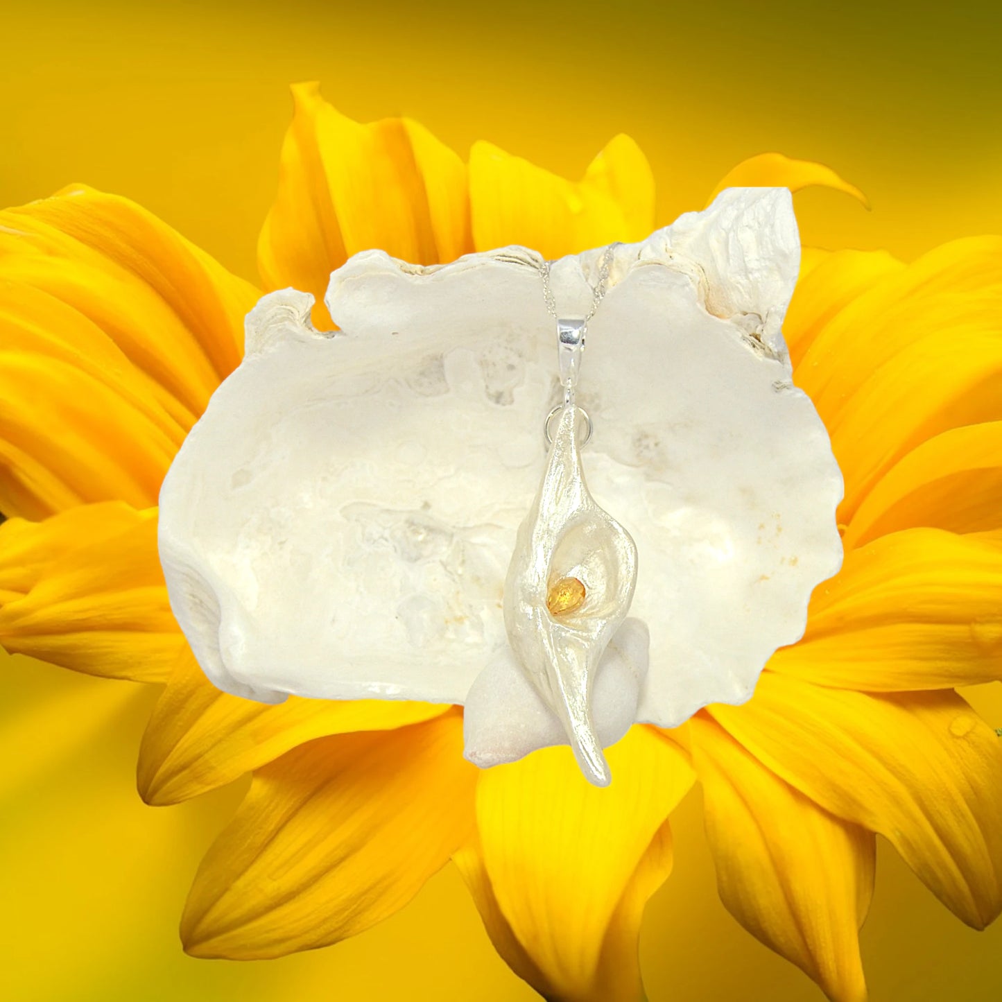 Lightmaker natural seashell pendant A beautiful pear shaped rose cut Citrine compliments the pendant. The pendant is shown hanging in front of a larger seashell and a yellow flower.