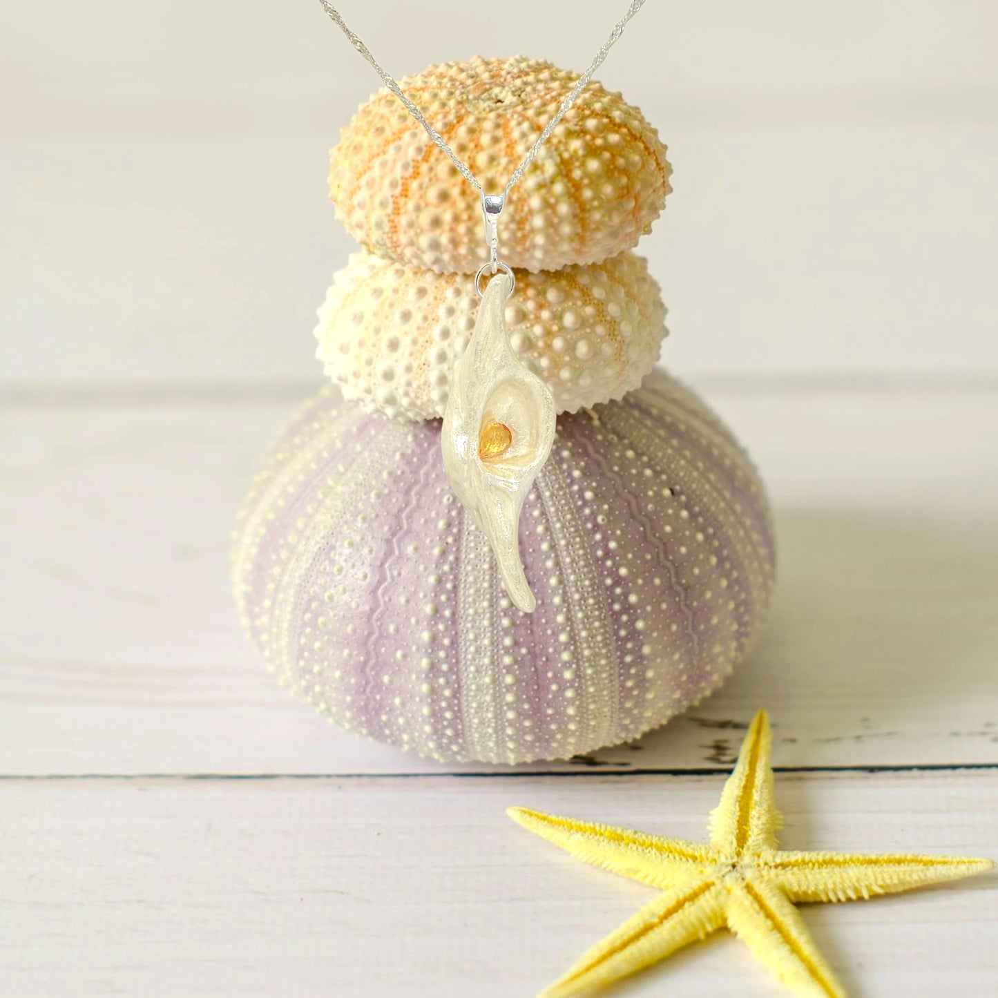 Lightmaker natural seashell pendant A beautiful pear shaped rose cut Citrine compliments the pendant. The pendant is shown hanging over top of three sea urchins and a starfish in front.