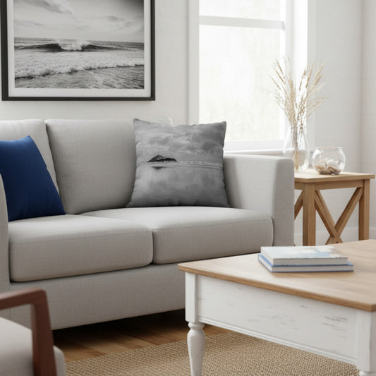 A throw pillow with a printed image of a coastal scene, featuring a pillow cover with a grayish-blue hue and a visible island in the distance.