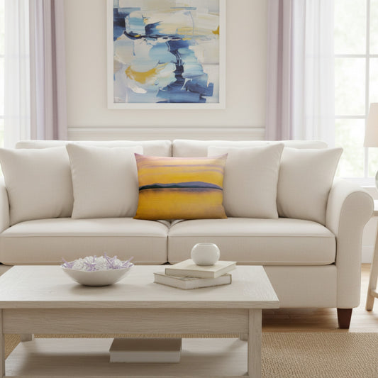 A cream-colored sofa in a bright, modern living room setting, styled with a square throw pillow featuring a yellow, pink, and blue abstract landscape design.