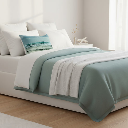 A neatly made bed in a bright bedroom setting, styled with white bedding, a sage green throw blanket, a matching green bed skirt, and a decorative teal and white striped accent pillow.
