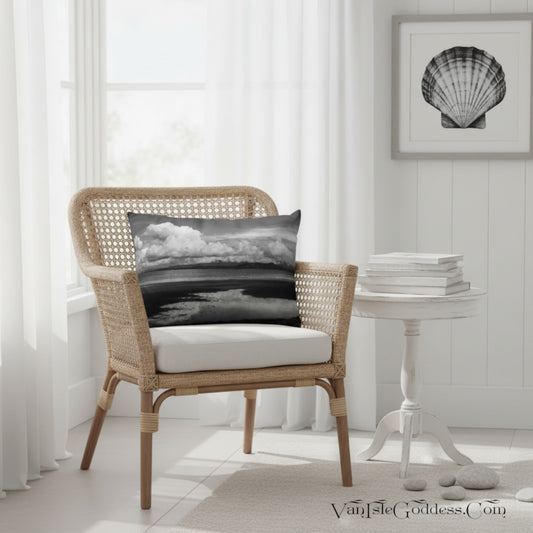 A black and white seashore landscape throw pillow displayed on a wicker armchair in a bright, modern room setting.