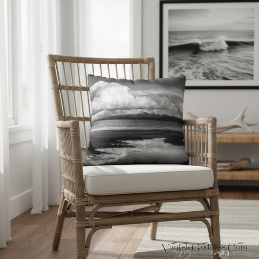 A square throw pillow with a black and white ocean wave print is styled on a rattan armchair in a bright, modern room.