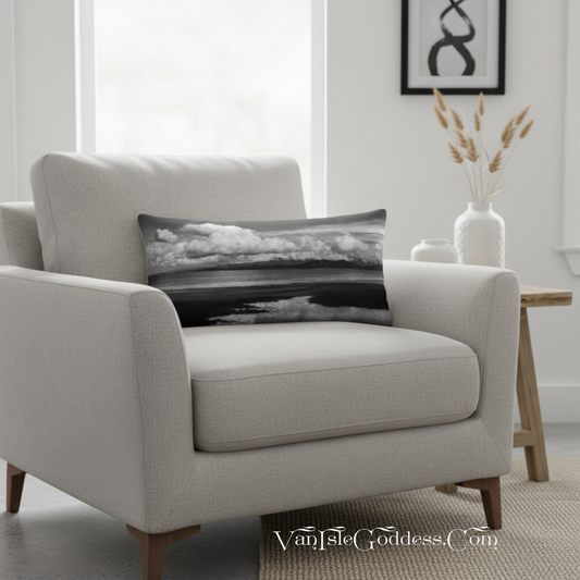 A rectangular lumbar throw pillow with a black and white landscape photograph of clouds and water, resting on a light beige armchair in a modern living room setting.