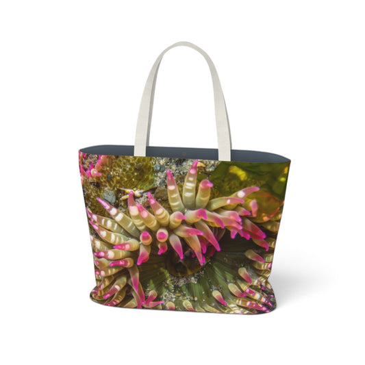 A tote bag featuring a close-up photograph of a sea anemone with pink and green tentacles, complete with white shoulder straps, shown on a plain white background.