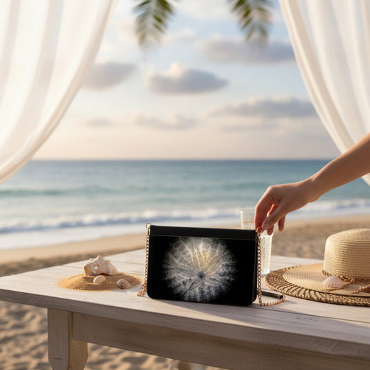 Hand holding a black clutch with a Sand Dollar design on a table by the beach.