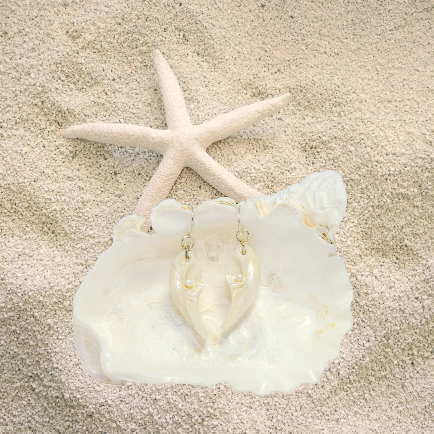 Seraphina natural seashell earrings with real baby freshwater pearls. The earrings are shown on the sand with a starfish.