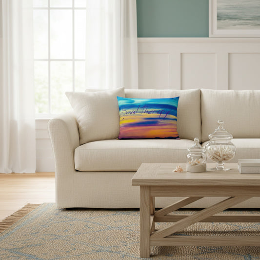 A square throw pillow with a colorful abstract sunset design in blue, orange, yellow, and purple, styled on a cream-colored sofa in a bright, modern living room.