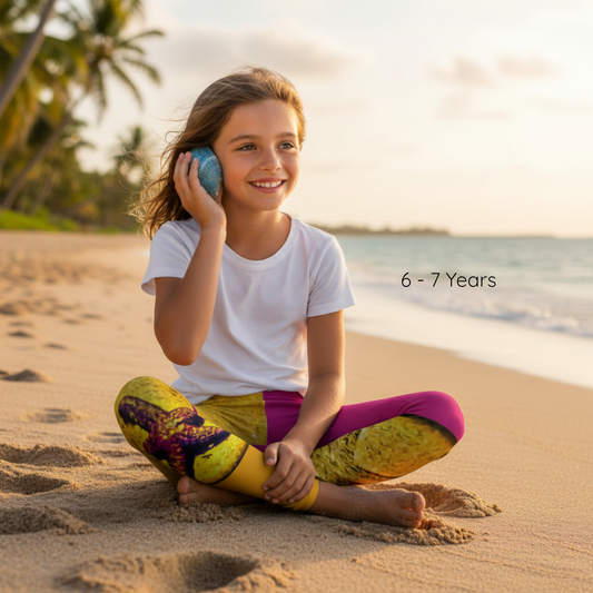 Young girl sitting on a beach holding a blue ball, with palm trees and ocean in the background.