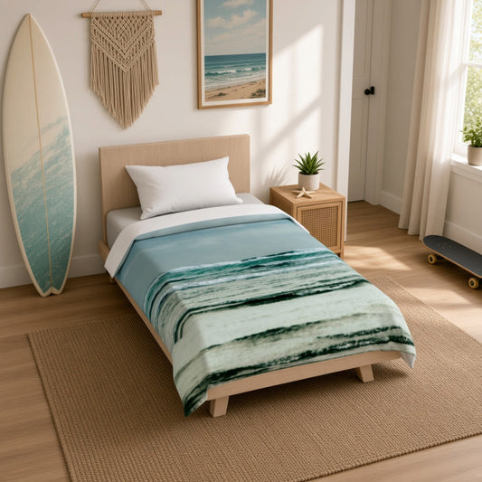 A single bed in a bright, modern bedroom styled with a light blue and teal watercolor-patterned blanket, white pillow, and a light wood headboard. The room features a beach-themed macrame wall hanging, a framed ocean print, a surfboard leaning against the wall, and a window with sheer curtains.