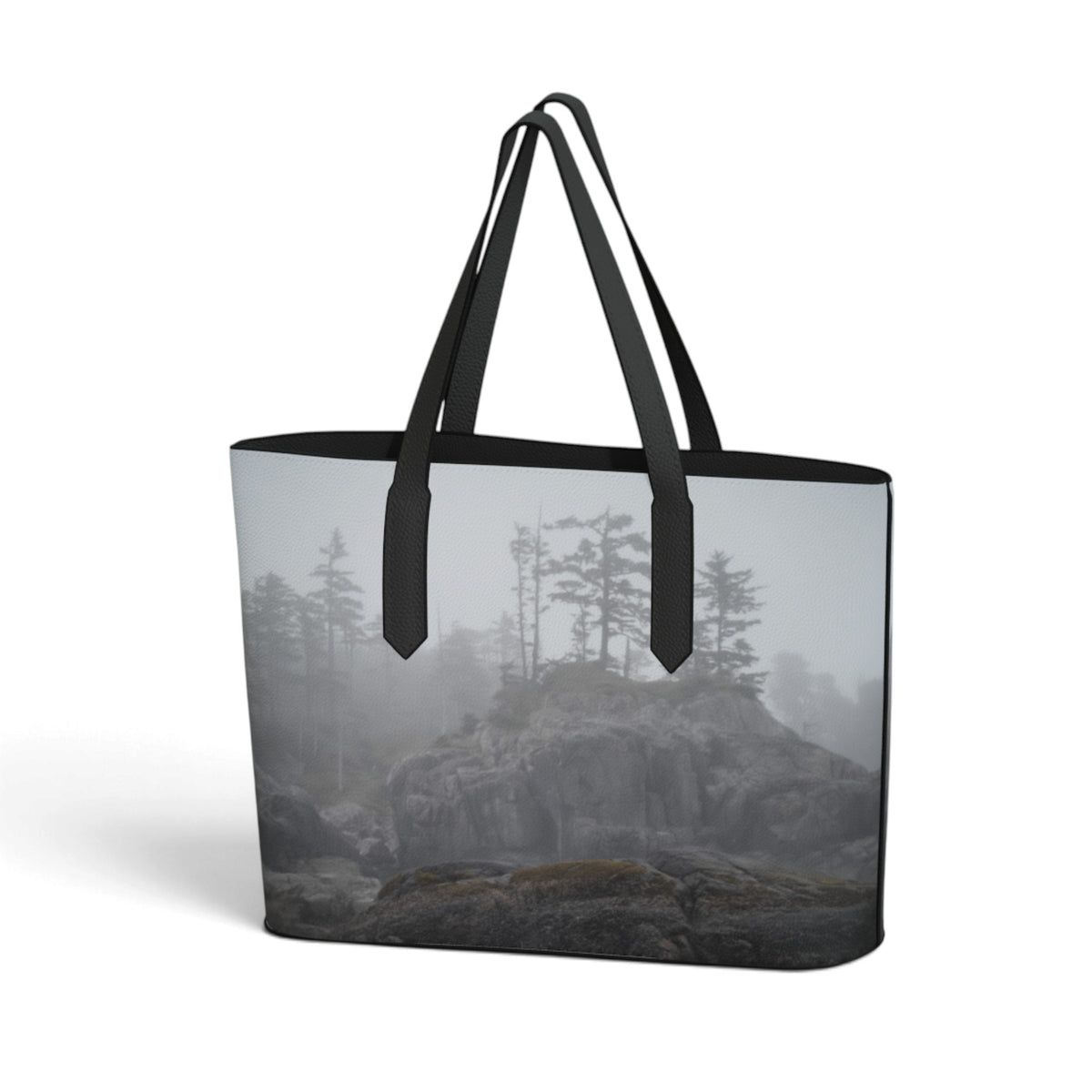 A tote bag featuring a printed landscape design of a foggy rocky cliff with pine trees, complete with black shoulder straps and black trim, shown on a plain white background.