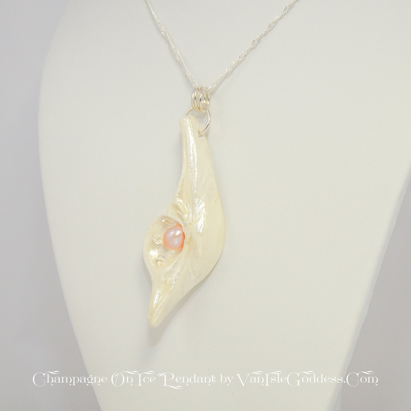 The Champagne on Ice pendant is shown hanging from a necklace. The pendant is slightly turned to show the left side of the pendant. The print on the bottom of the image says: champagne on ice pendant by van isle goddess dot com