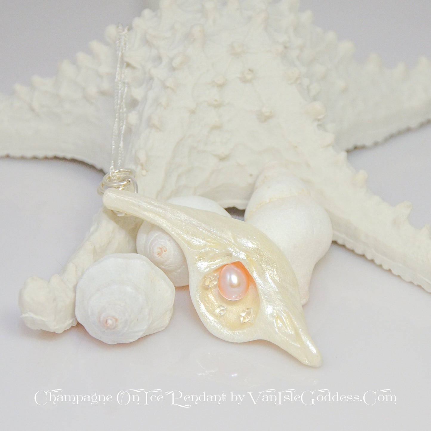 The pendant Champagne on Ice by Van Isle Goddess dot com is shown propped up against a few shells and a starfish.