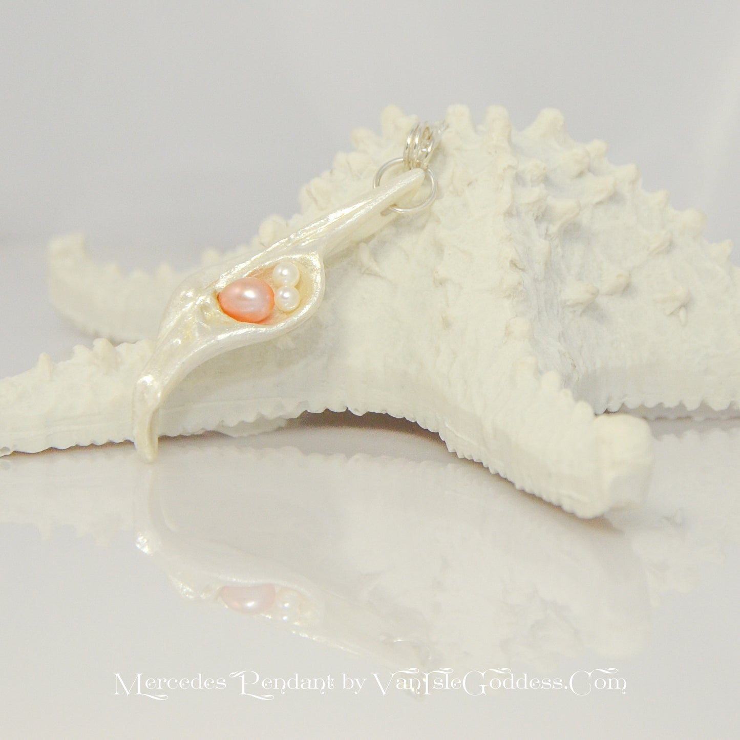 This natural seashell pendant has a real 7-8mm pink freshwater pearl and two baby pearls. The pendant is shown resting a a starfish. The words printed on the bottom read: Mercedes Pendant by Van Isle Goddess dot com