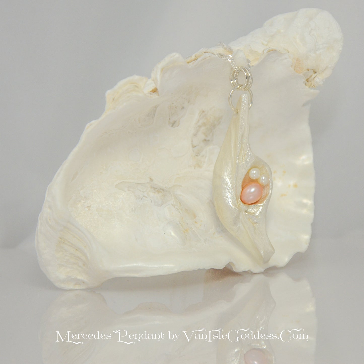 This natural seashell pendant has a real 7-8mm pink freshwater pearl and two baby pearls. The pendant is shown in front of a larger seashell. The words on the bottom of the image read: Mercedes Pendant by Van Isle Goddess dot com