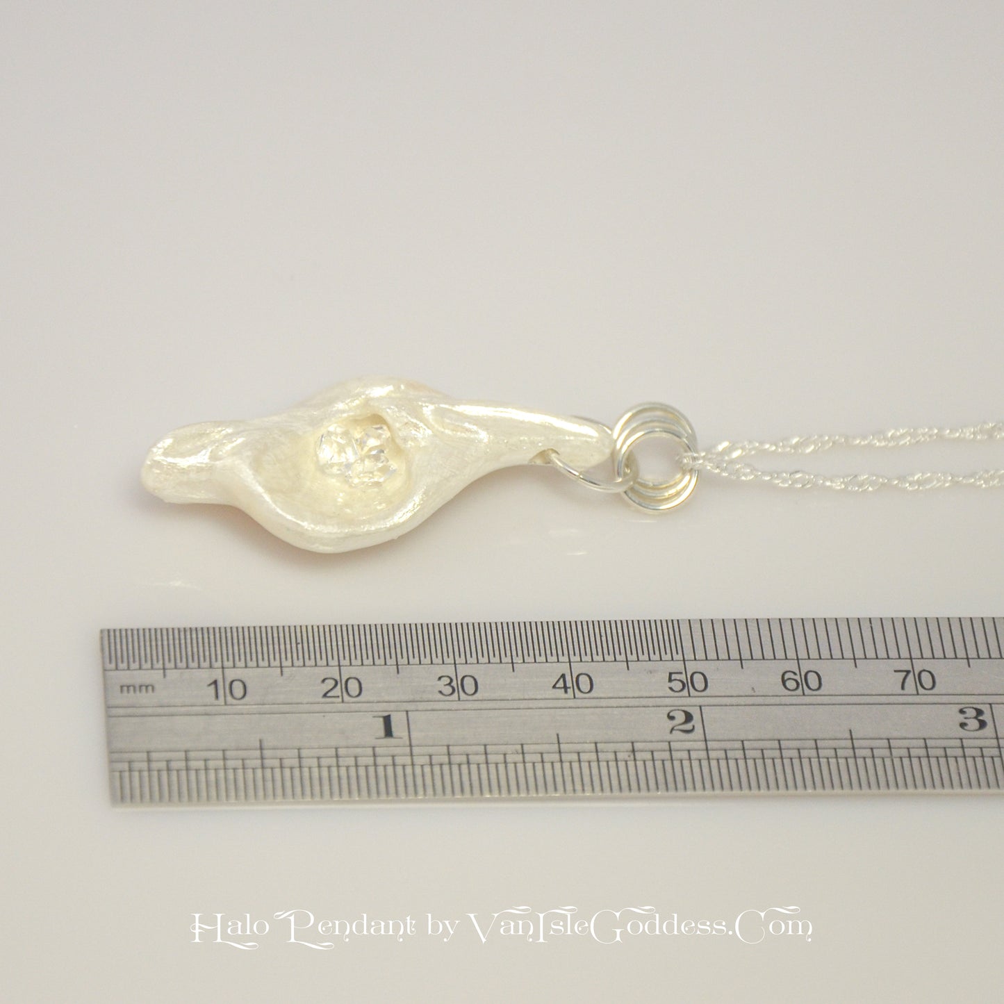 Halo natural seashell pendant with three herkimer diamonds. The pendant is shown laying along a ruler so the viewer can see the length of the pendant.