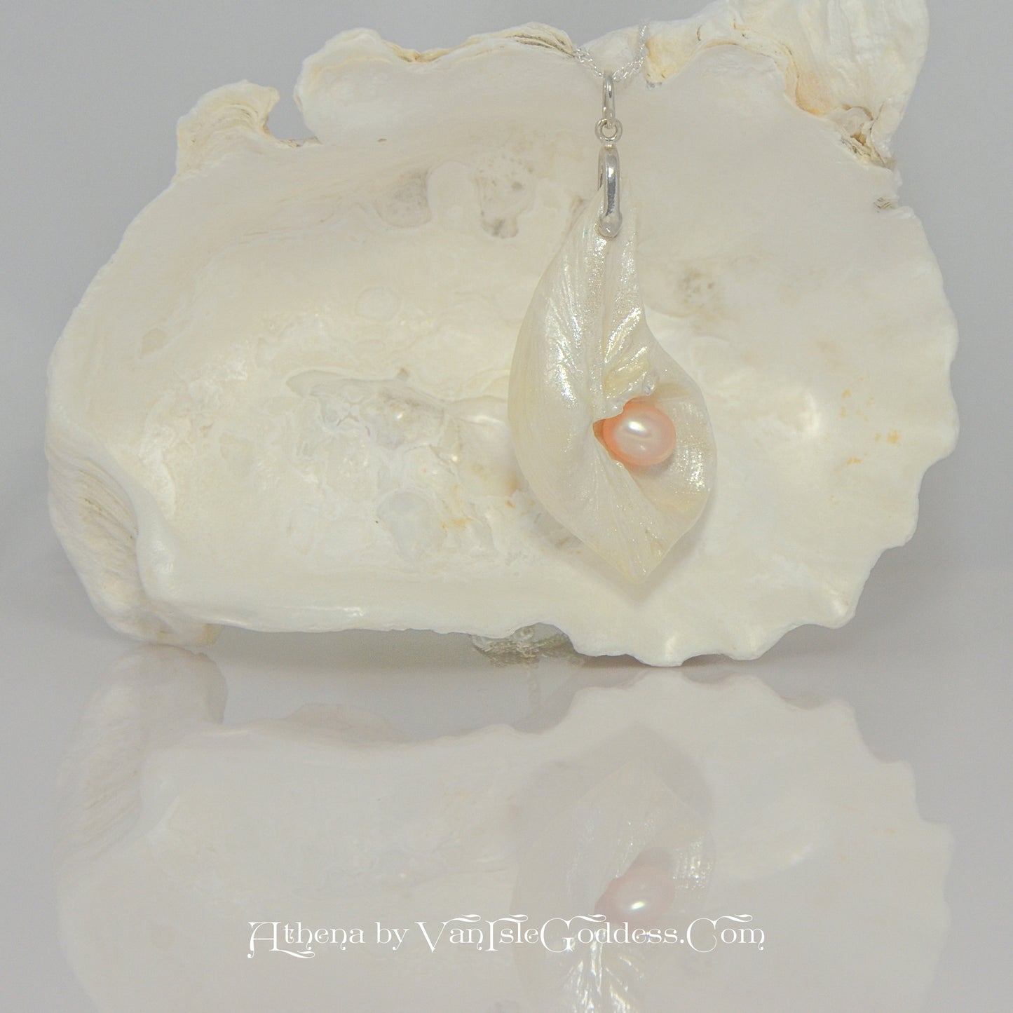 Athena is the name of the pendant being showcased. It is a natural seashell from the beaches of Vancouver Island. The pendant has a real pink freshwater pearl and a faceted herkimer diamond. The pendant is hanging on a large seashell to show how the pendant will hang.