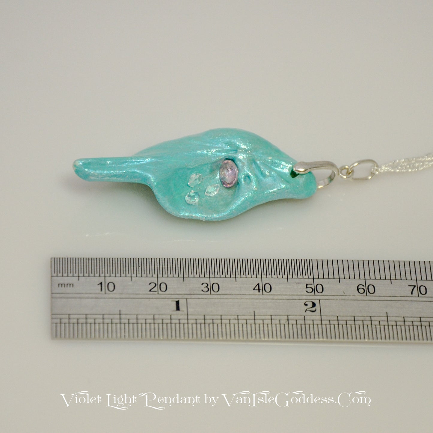 Violet Light is a natural seashell pendant with a rose cut Amethyst Gemstone and three Herkimer diamonds. The pendant is shown along a ruler so the viewer can see the length of the pendant.