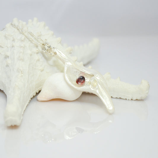Pomegranate natural seashell pendant is adorned with a stunning Garnet gemstone. the pendant rests against a starfish.