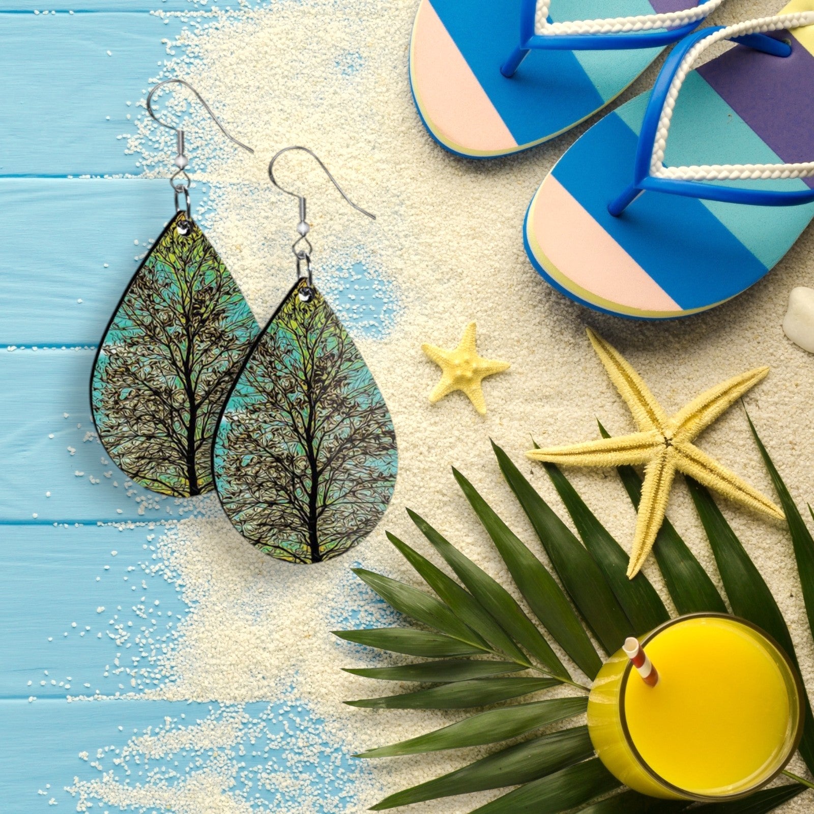 Teardrop-shaped earrings with nature design on a beach-themed background with flip-flops, starfish, and a drink.