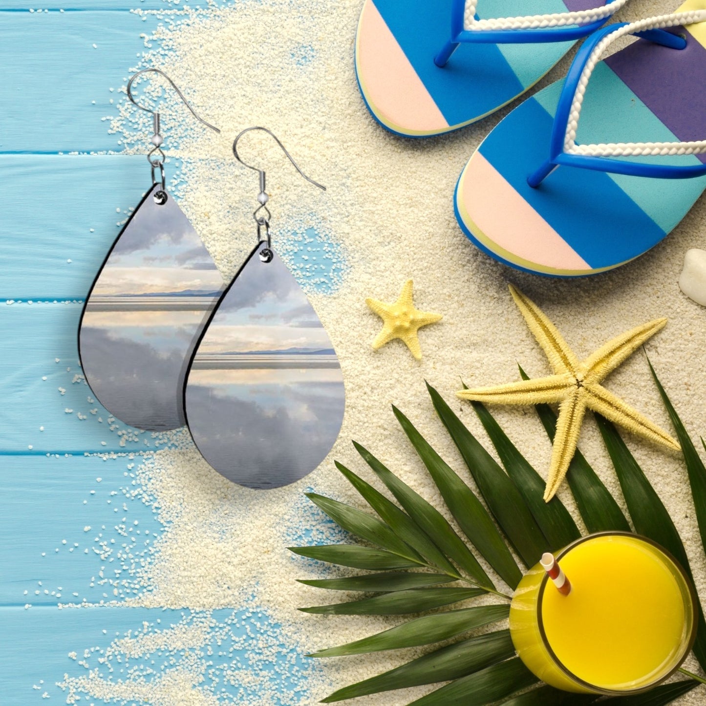 Teardrop-shaped earrings on a beach-themed background with flip-flops, starfish, and a drink.