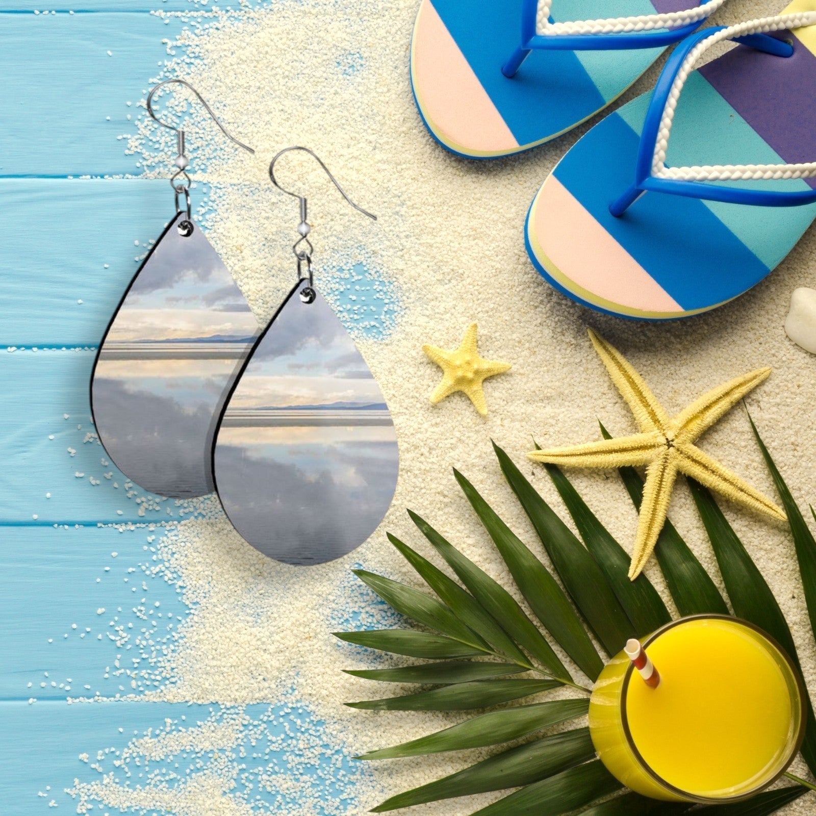 Teardrop-shaped earrings on a beach-themed background with flip-flops, starfish, and a drink.