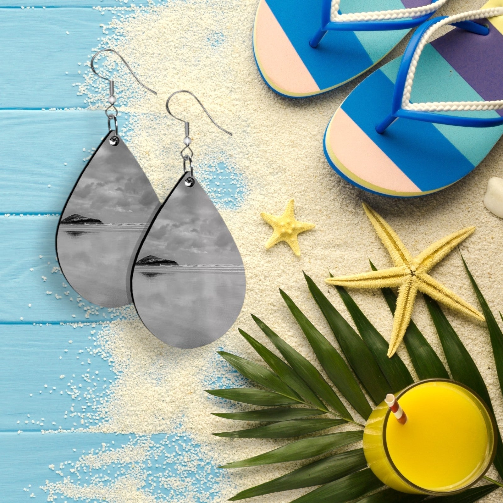 Gray teardrop earrings on a beach-themed background with flip-flops, starfish, and a drink.