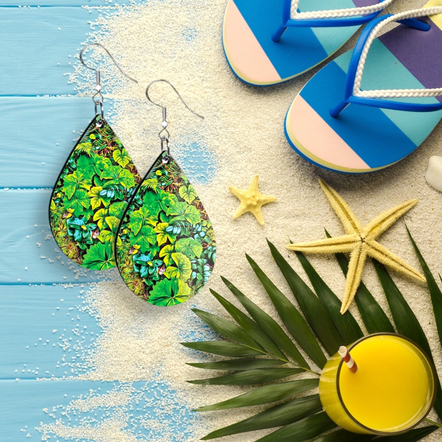 Colorful earrings on a sandy surface with flip-flops, starfish, and a drink.