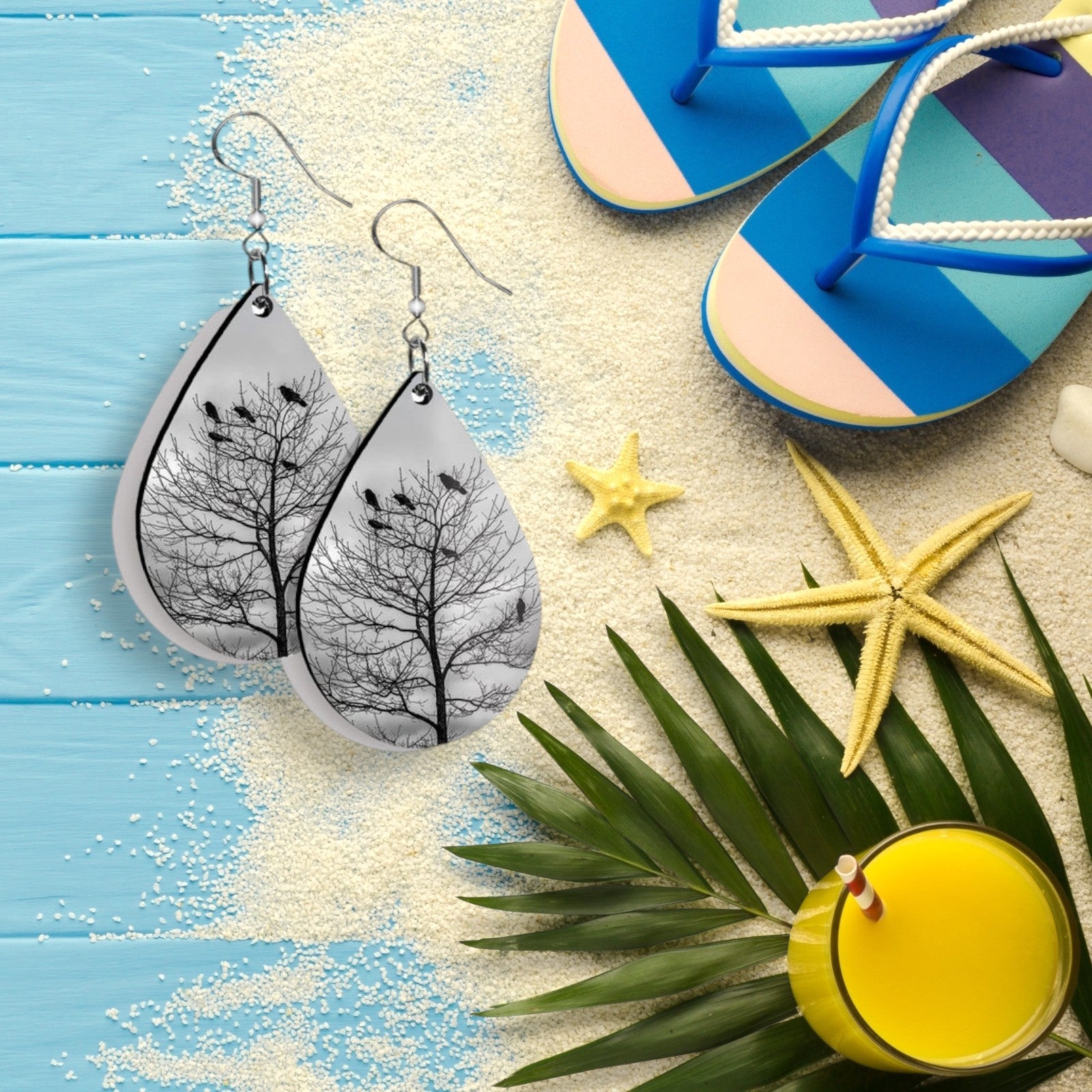 Teardrop-shaped earrings with tree design on a beach-themed background with flip-flops, starfish, and a drink.