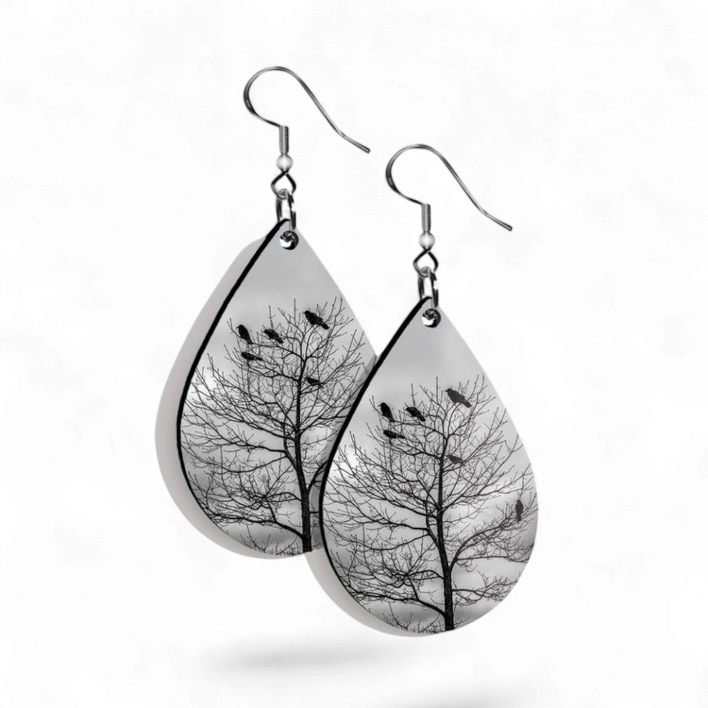 Teardrop-shaped earrings with tree and bird design on a white background