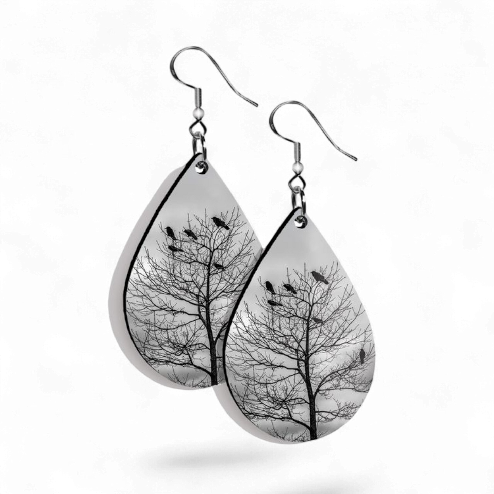 Teardrop-shaped earrings with tree and bird design on a white background