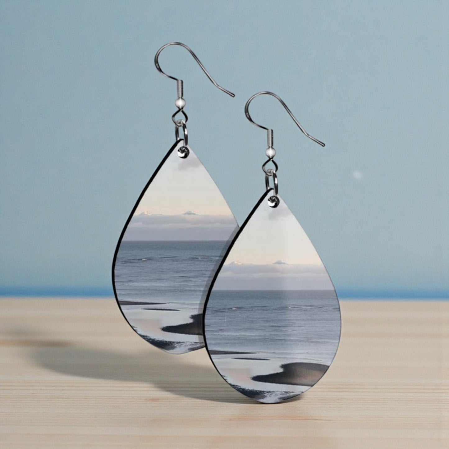 Teardrop-shaped earrings with ocean scene design on a wooden surface and blue background