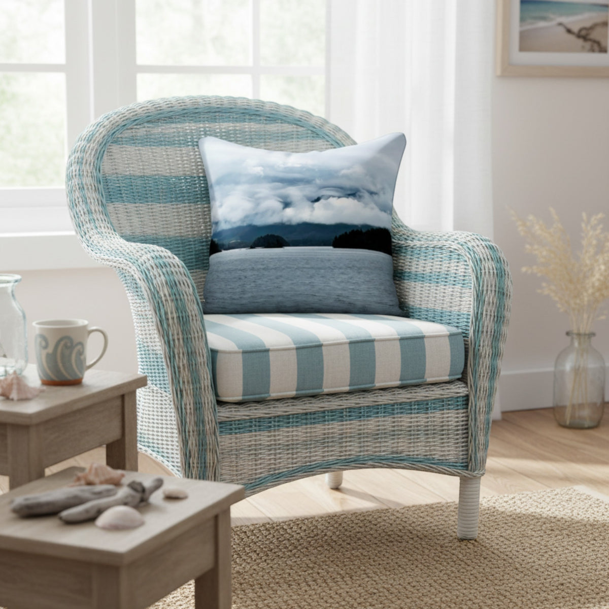 A woven outdoor-style armchair with a light blue and white striped cushion, styled in a bright room with two decorative throw pillows. A small wooden side table is on the left, and a window is in the background.