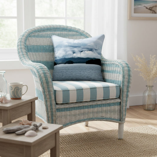 A woven outdoor-style armchair with a light blue and white striped cushion, styled in a bright room with two decorative throw pillows. A small wooden side table is on the left, and a window is in the background.