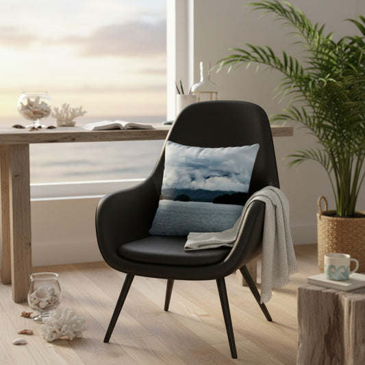 A black mid-century modern armchair in a bright, coastal-styled room, featuring a blue and white cloud-patterned throw pillow and a draped light gray throw blanket.