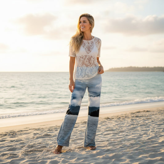Woman standing on a beach wearing a white lace top and patterned pants.