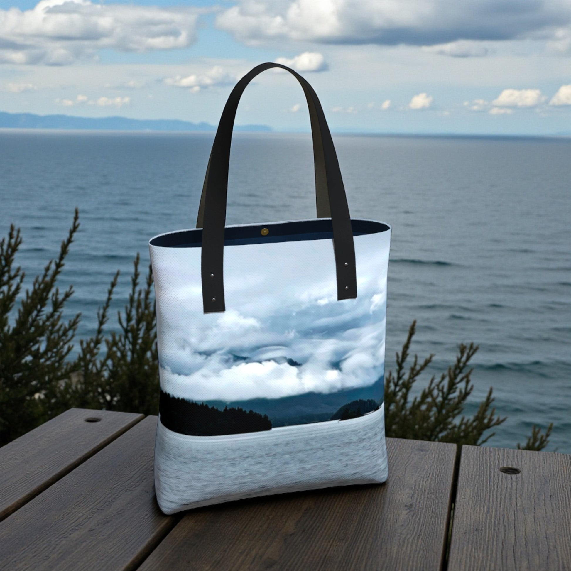 Tote bag with a scenic design of clouds e trees on a wooden surface by the ocean.