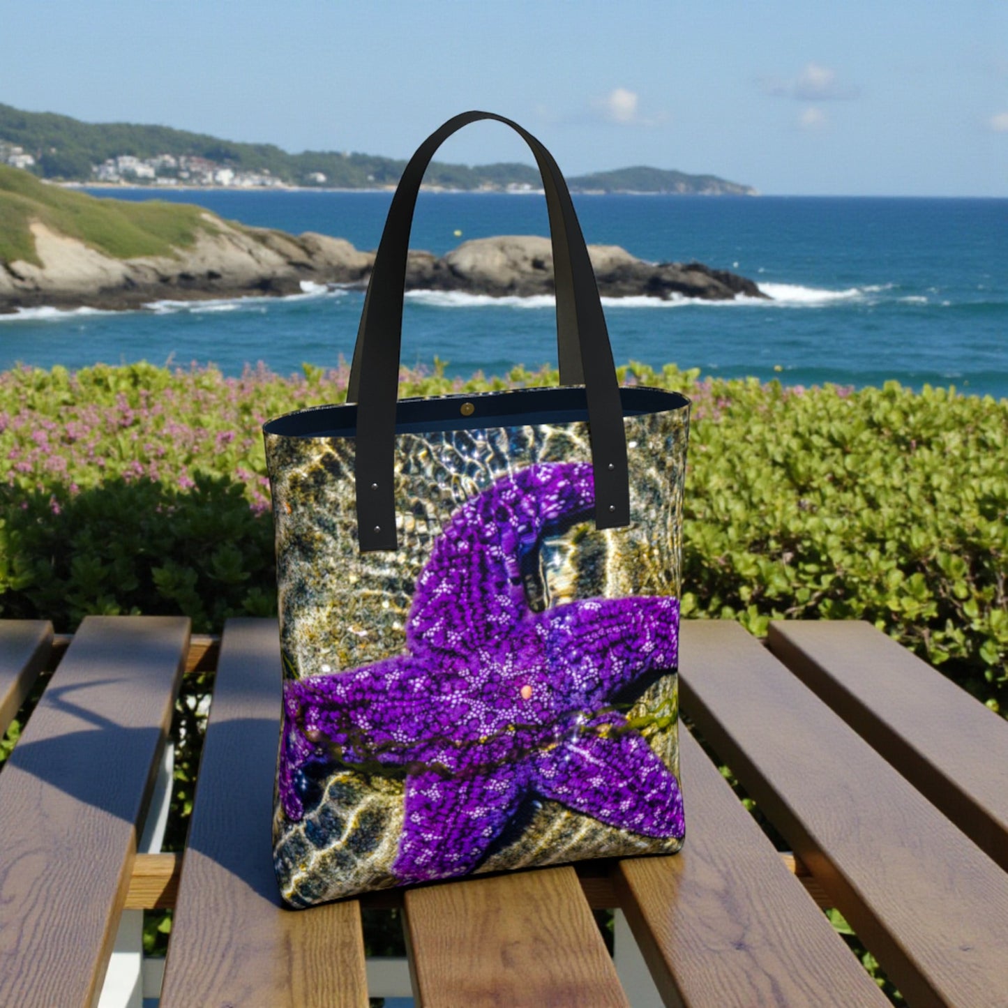 Tote bag with a purple starfish  design on a wooden bench by the ocean.