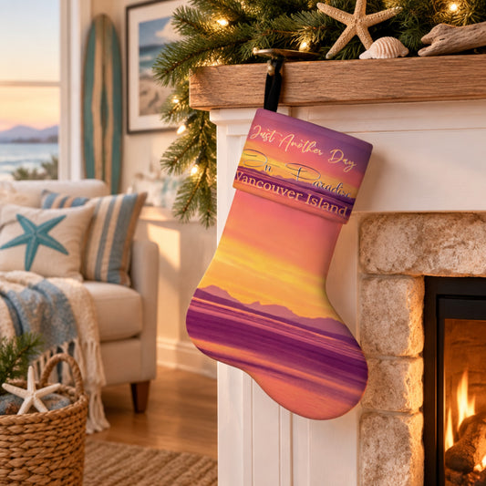 A Christmas stocking hanging from a wooden fireplace mantel in a cozy living room. The stocking features a printed sunset landscape of Vancouver Island with purple mountains, a yellow and orange sky, and a purple cuff that reads 'Just Another Day on Vancouver Island'.