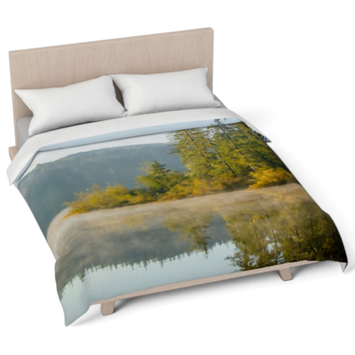 A bed dressed with a printed comforter featuring a misty lake reflection scene with green and yellow trees, styled with two white pillows against a light wood headboard on a white background.