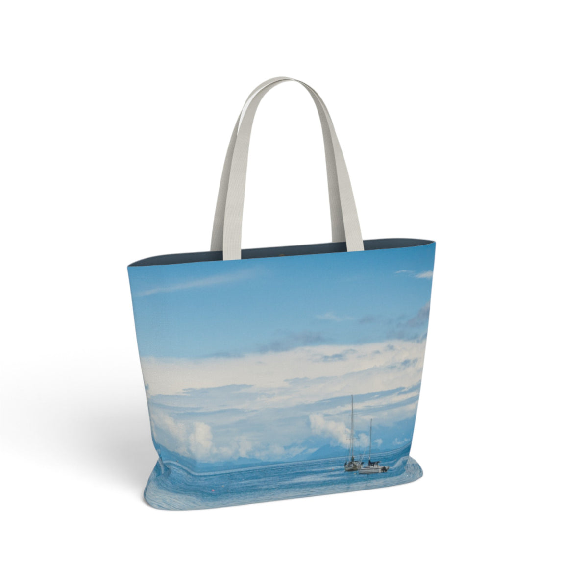 A tote bag featuring a scenic print of a sailboat on a blue ocean under a cloudy sky, with light gray fabric handles, shown on a white background.