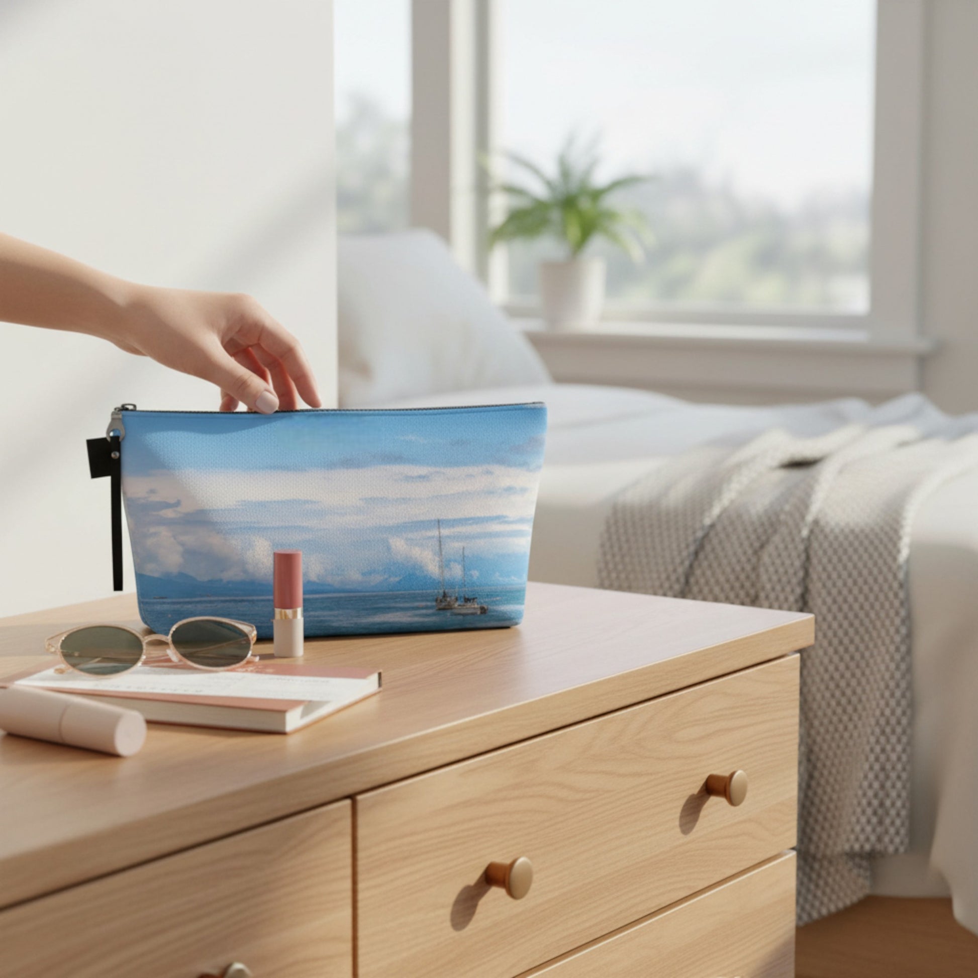 Hand reaching for a blue pouch with a scenic design on a wooden dresser.