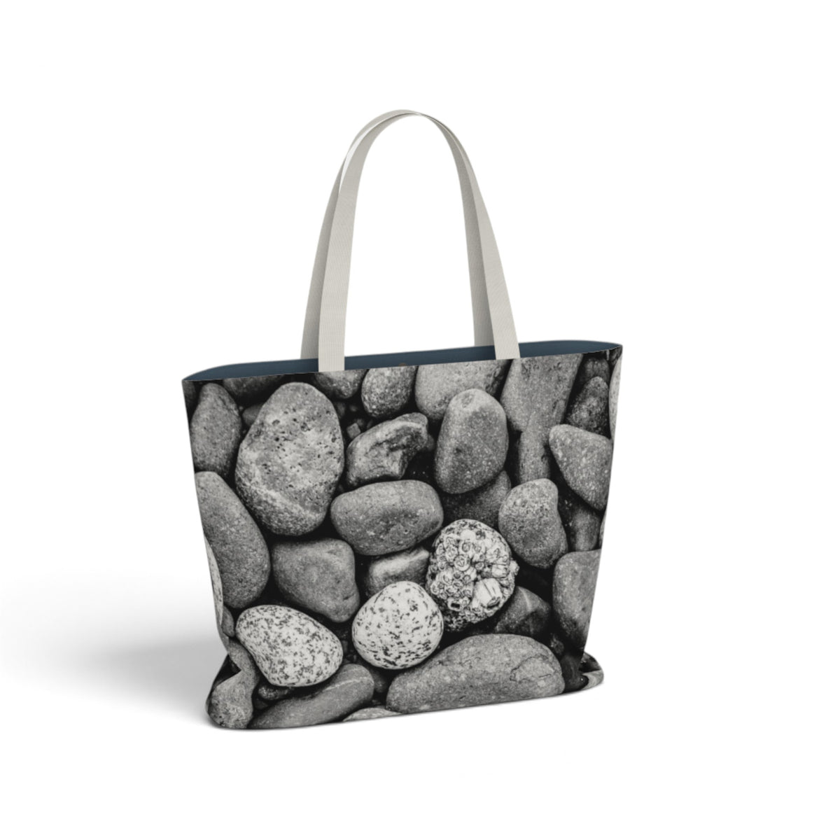 A tote bag featuring a black and white photograph of smooth river stones, with light gray fabric shoulder straps, shown on a plain white background.