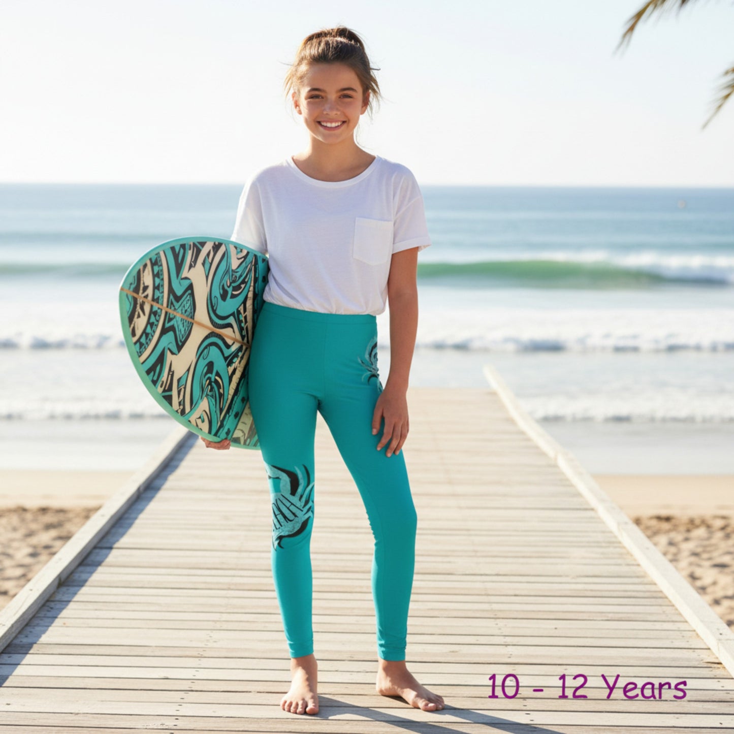 Child holding a surfboard on a wooden pier by the ocean, wearing teal leggings and a white shirt.