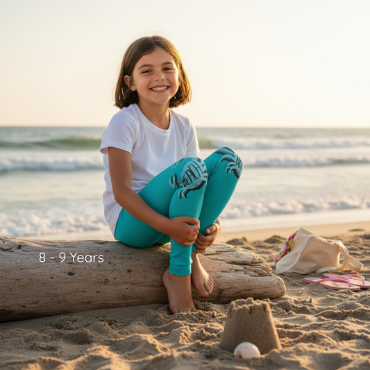 Young girl sitting on a log at the beach with sandcastle and bag in the background