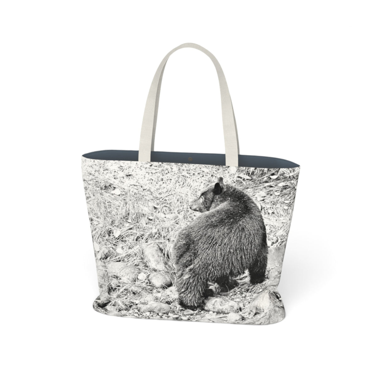 A tote bag featuring a black and white photographic print of a bear on a forest floor, with light beige fabric handles and a dark navy blue interior lining, shown against a plain white background.